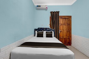 Una cama individual con una colcha blanca y negra, un cabecero floral azul y dos almohadas negras con un listón color beige.