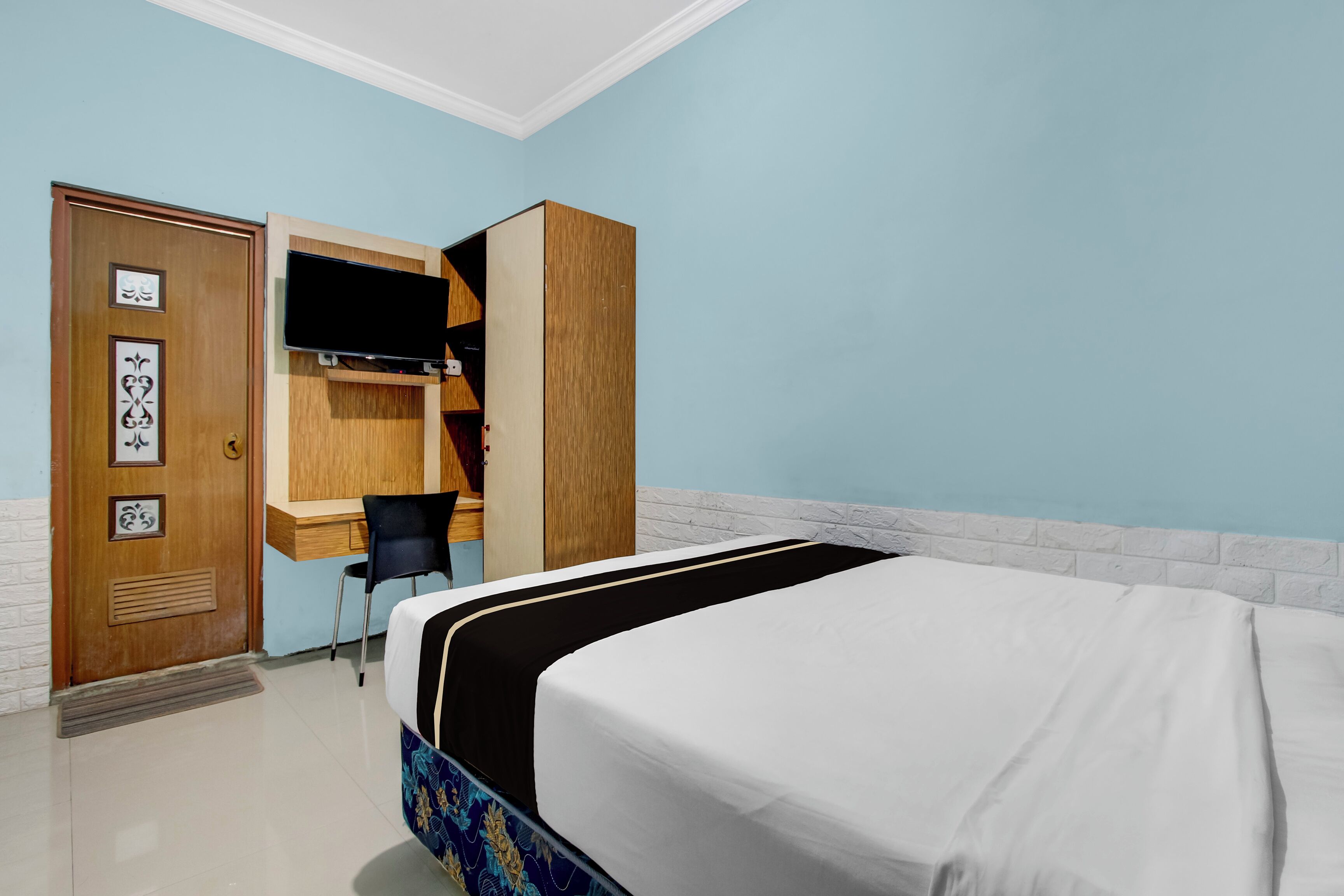 Una habitación de hotel con cama, escritorio y silla, y un armario.