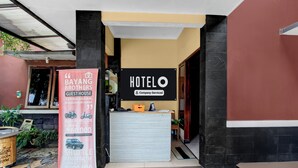 Entrada de hotel con recepción, cartel de casa de huéspedes y anuncio de servicio de transporte.