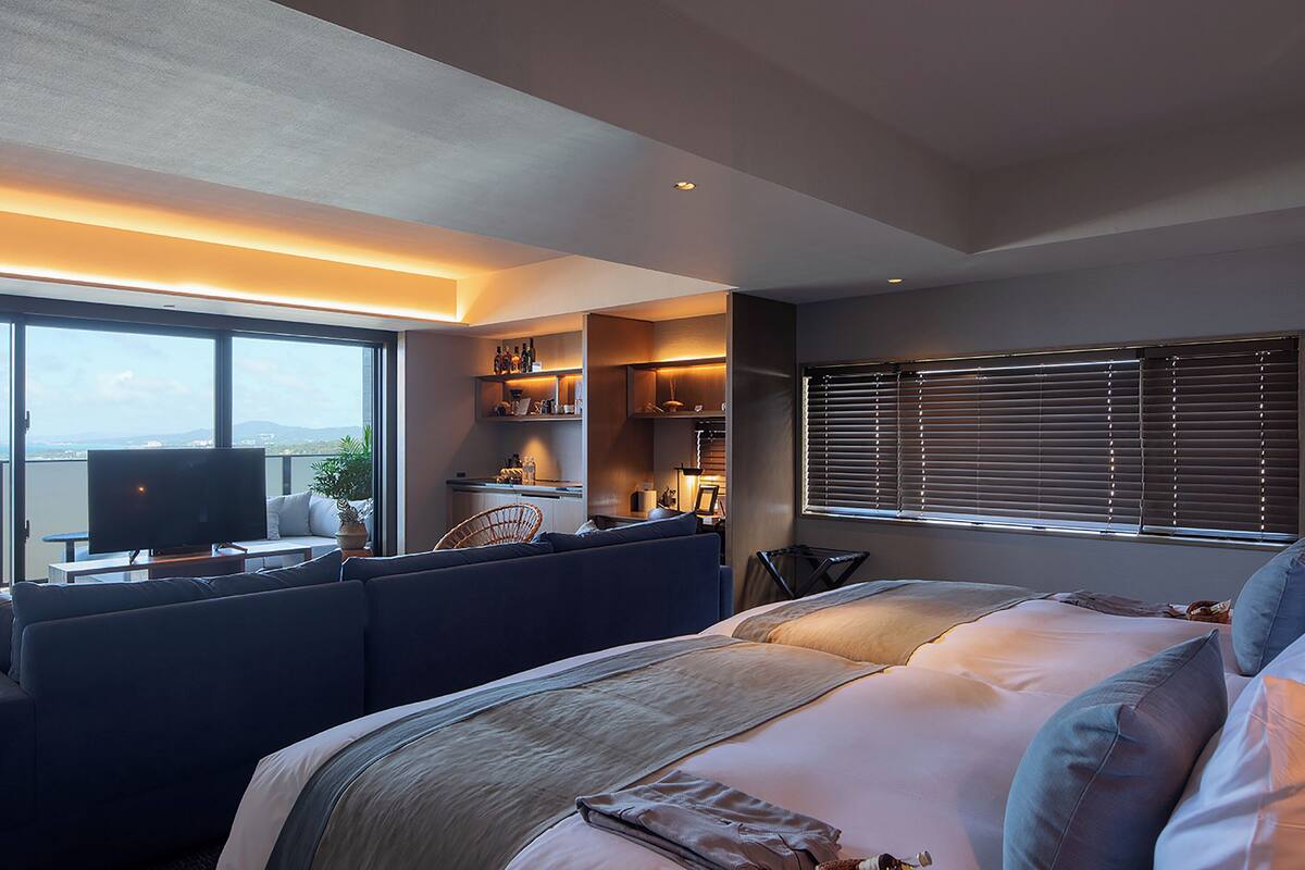 A modern hotel room with a large bed, a seating area with a TV, and a balcony with a view.