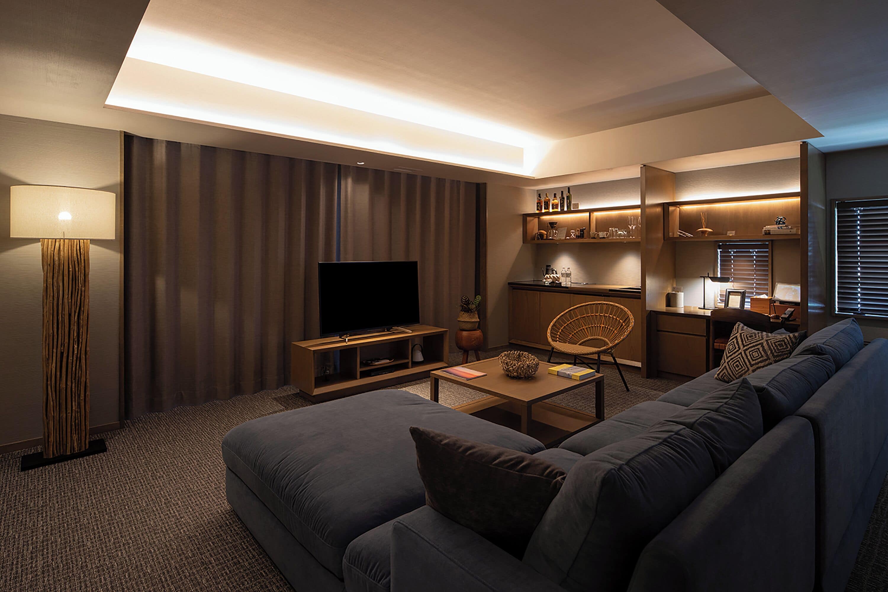 A modern living room with a large flat-screen TV, a sofa, a coffee table, and a lamp.