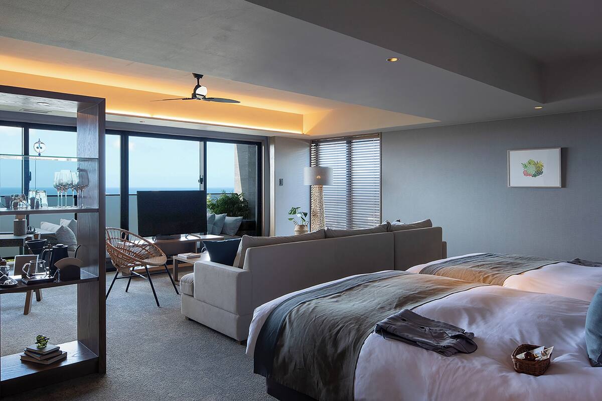 A modern hotel room with a large bed, a sofa, a dining area, and a view of the ocean.