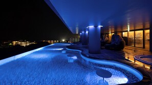 A modern outdoor pool area with a water feature, seating, and a view of the city at night. - Glamday Style Hotel & Resort Okinawa Yomitan (Yomitan)