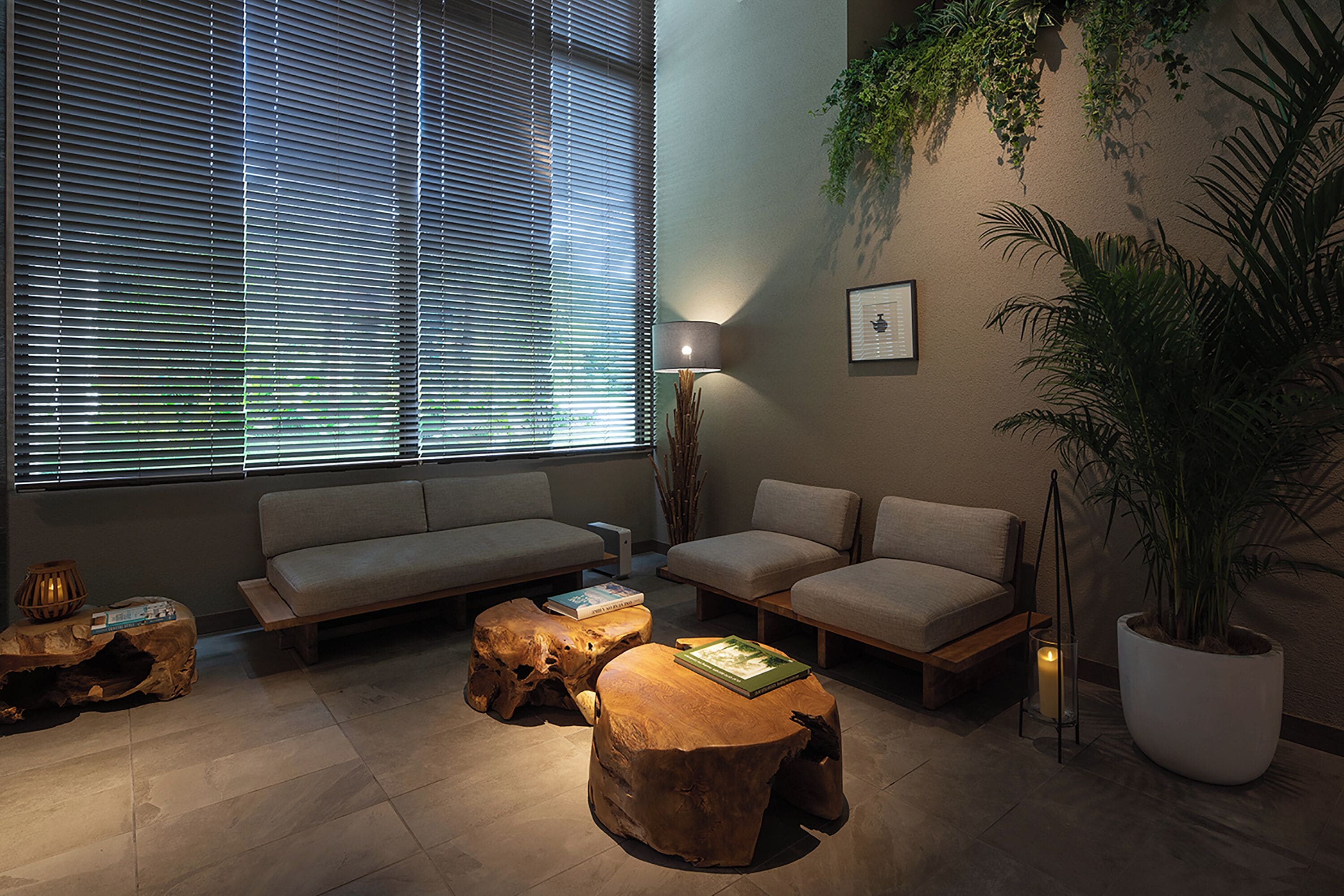 A modern living room with a sofa, two wooden coffee tables, a floor lamp, and a large potted plant.