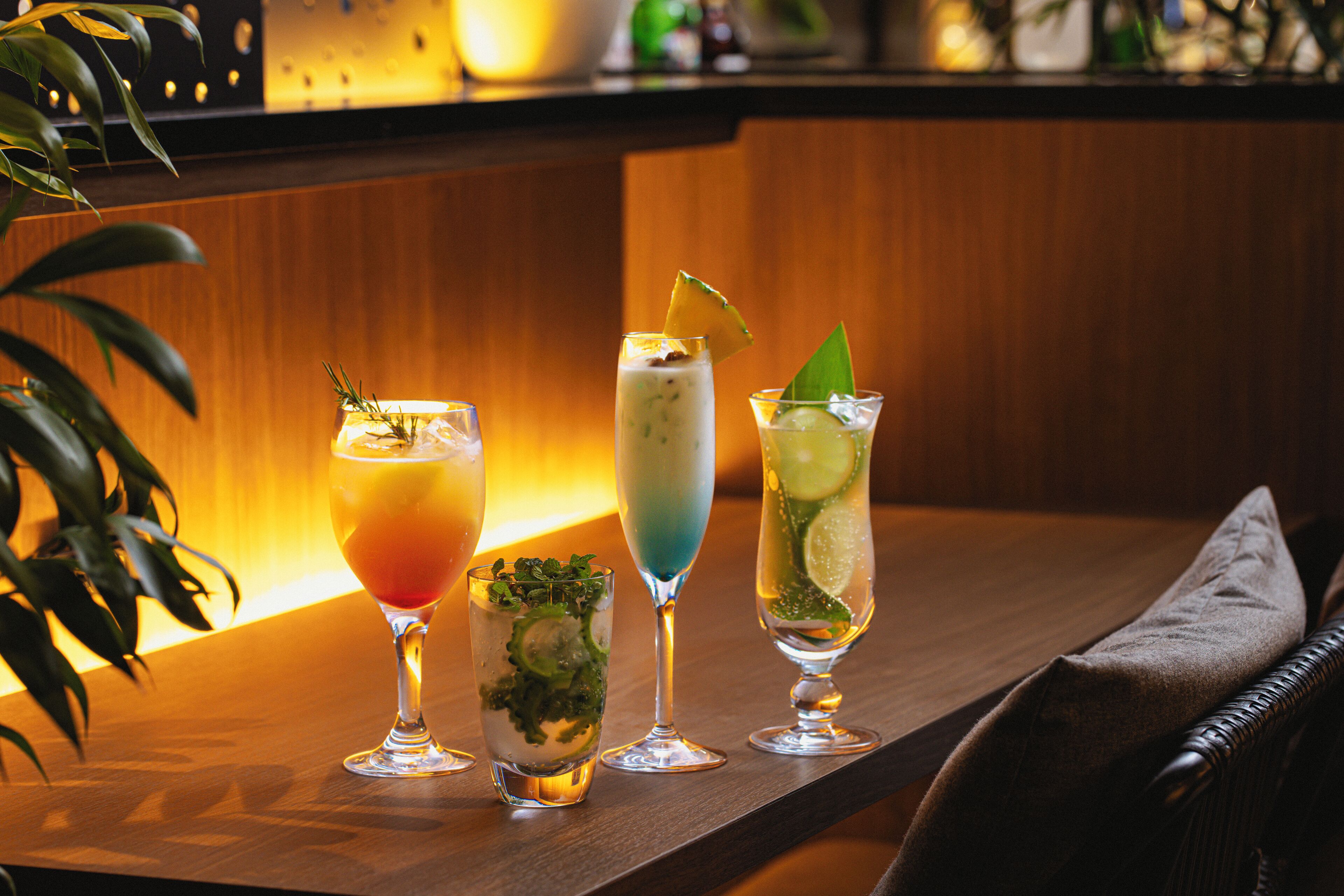 Drie cocktails op een houten bartafel, met een plant aan de linkerkant.