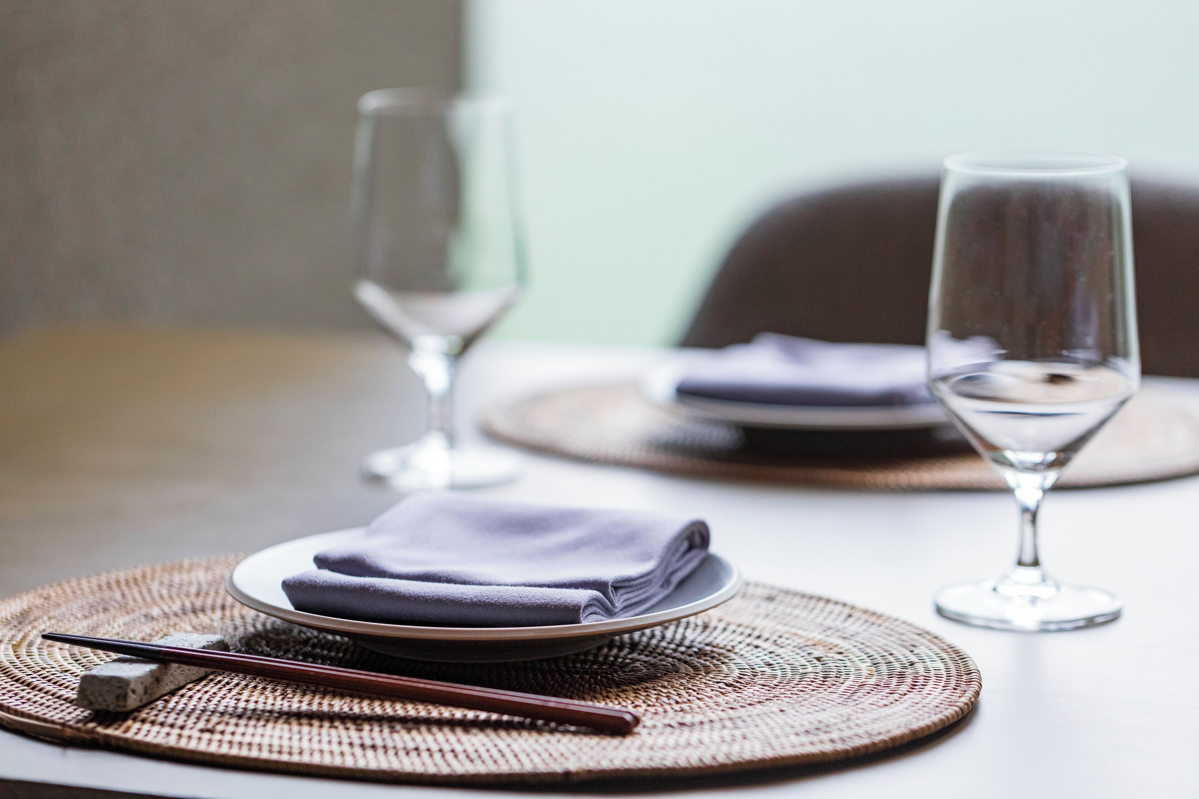 A dining table with a folded napkin, a pair of chopsticks, and two empty wine glasses.