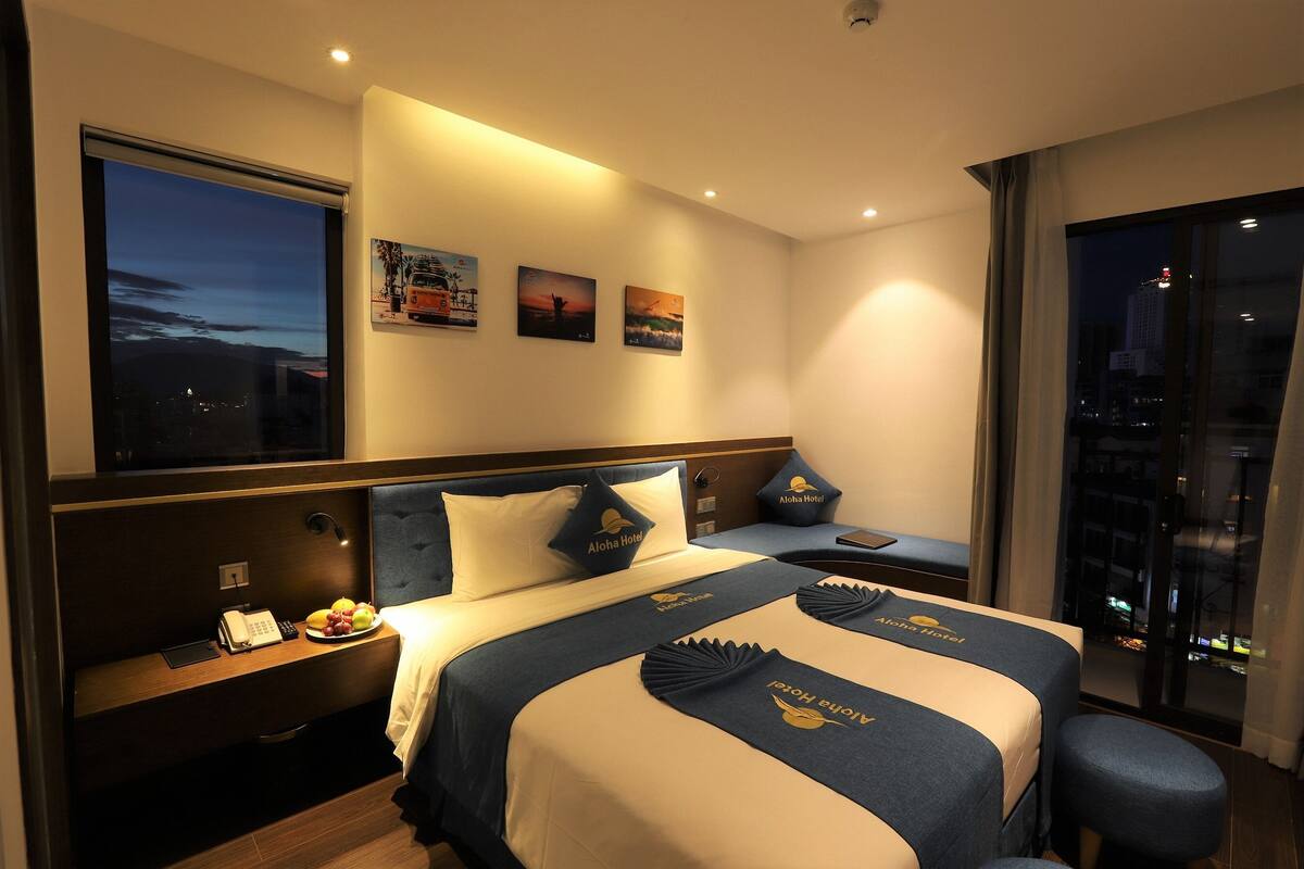 A hotel room with a large bed, a desk with a phone, and a view of the city at night.