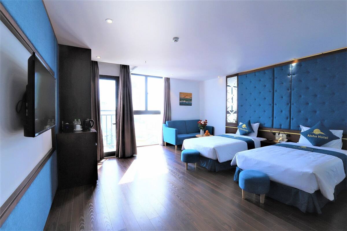 A hotel room with two beds, a sofa, a TV, and a coffee machine.