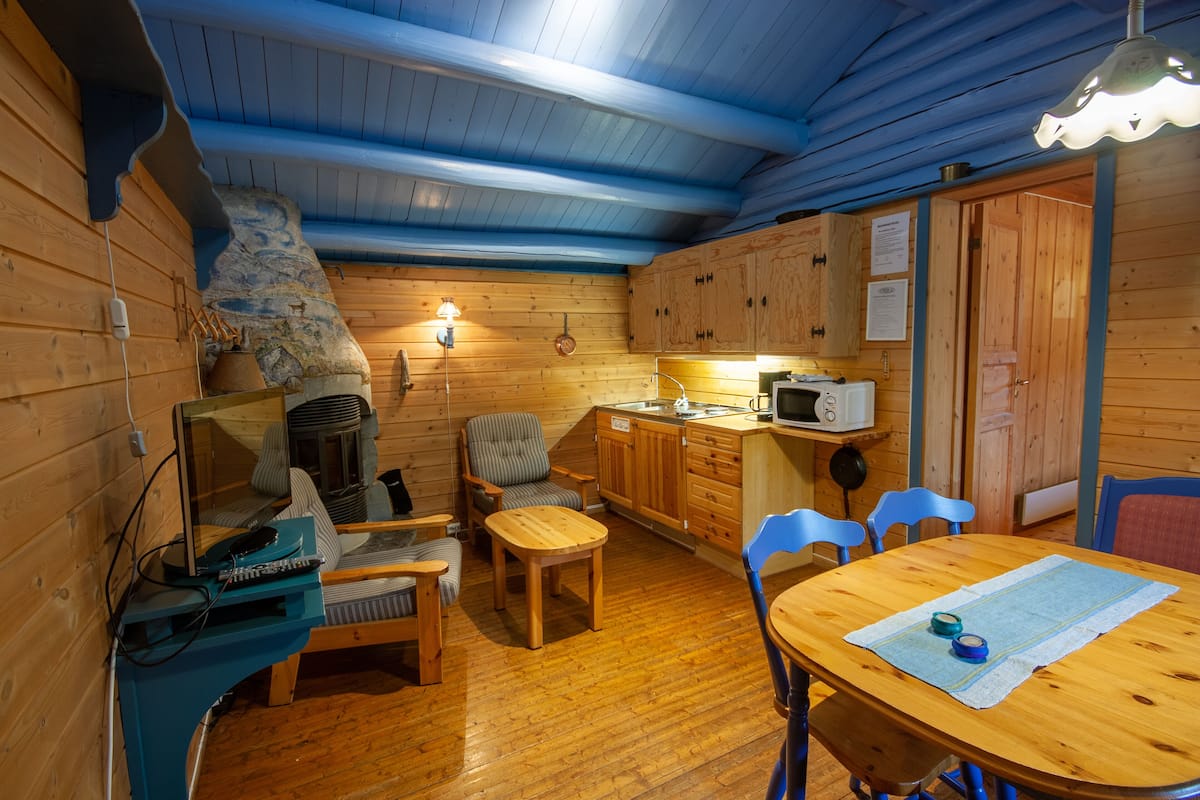 A cozy cabin interior with a fireplace, wooden furniture, a dining table, and a kitchen area.