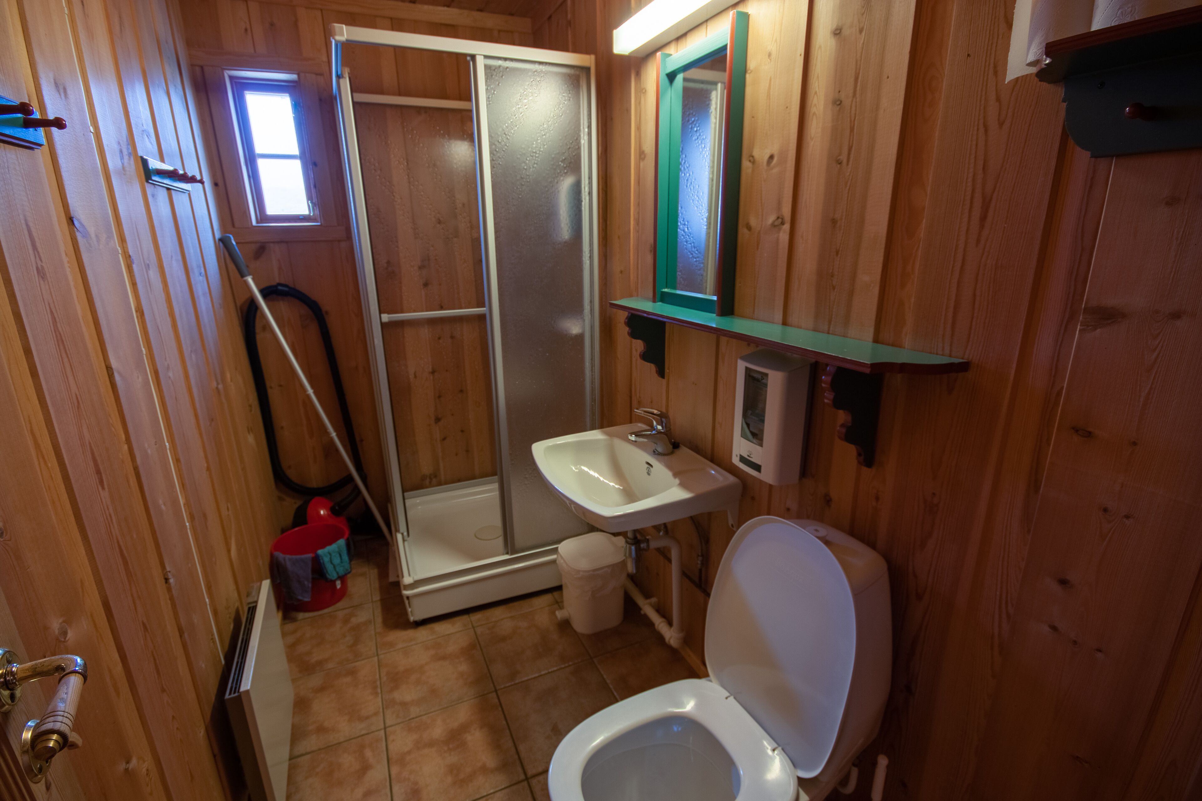 Un baño de madera con ducha, inodoro, lavamanos y un ventanal.