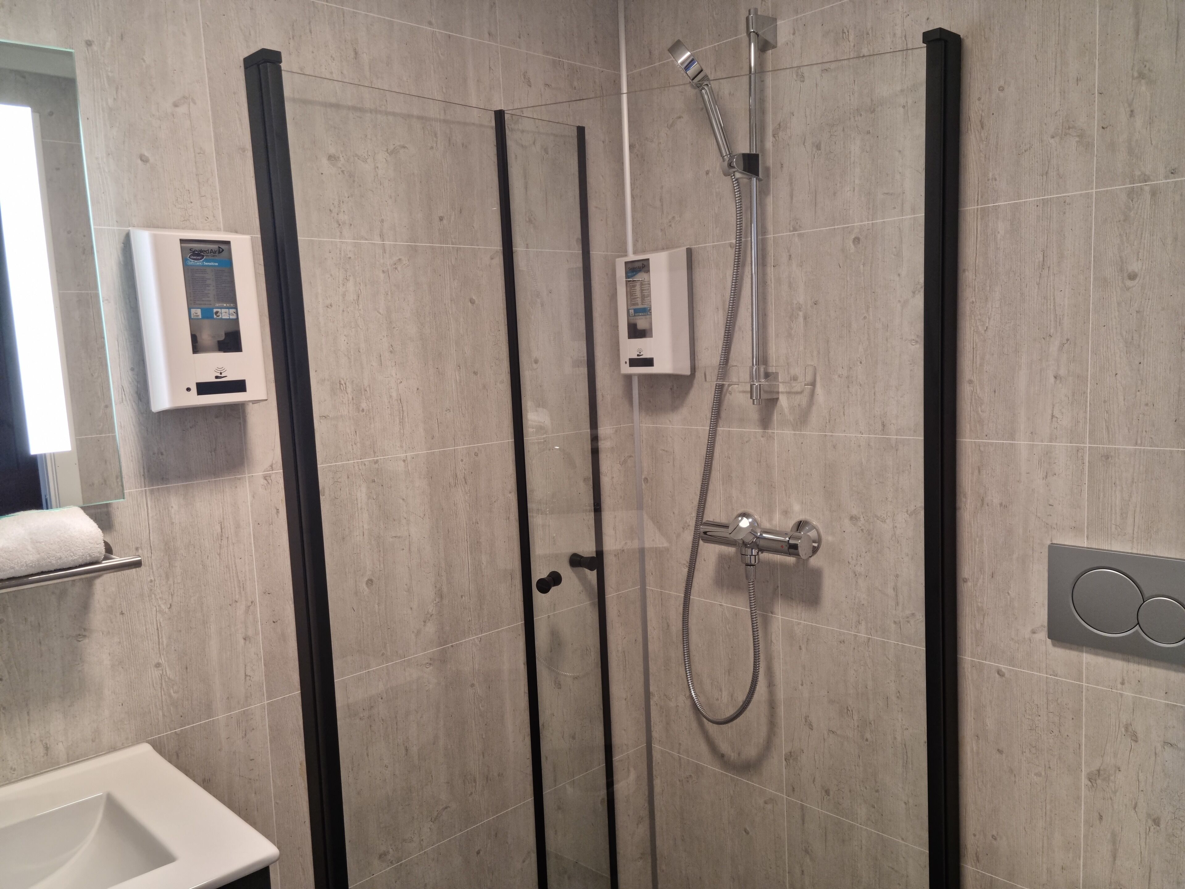 A modern bathroom with a glass-enclosed shower, a white sink, and a towel rack.