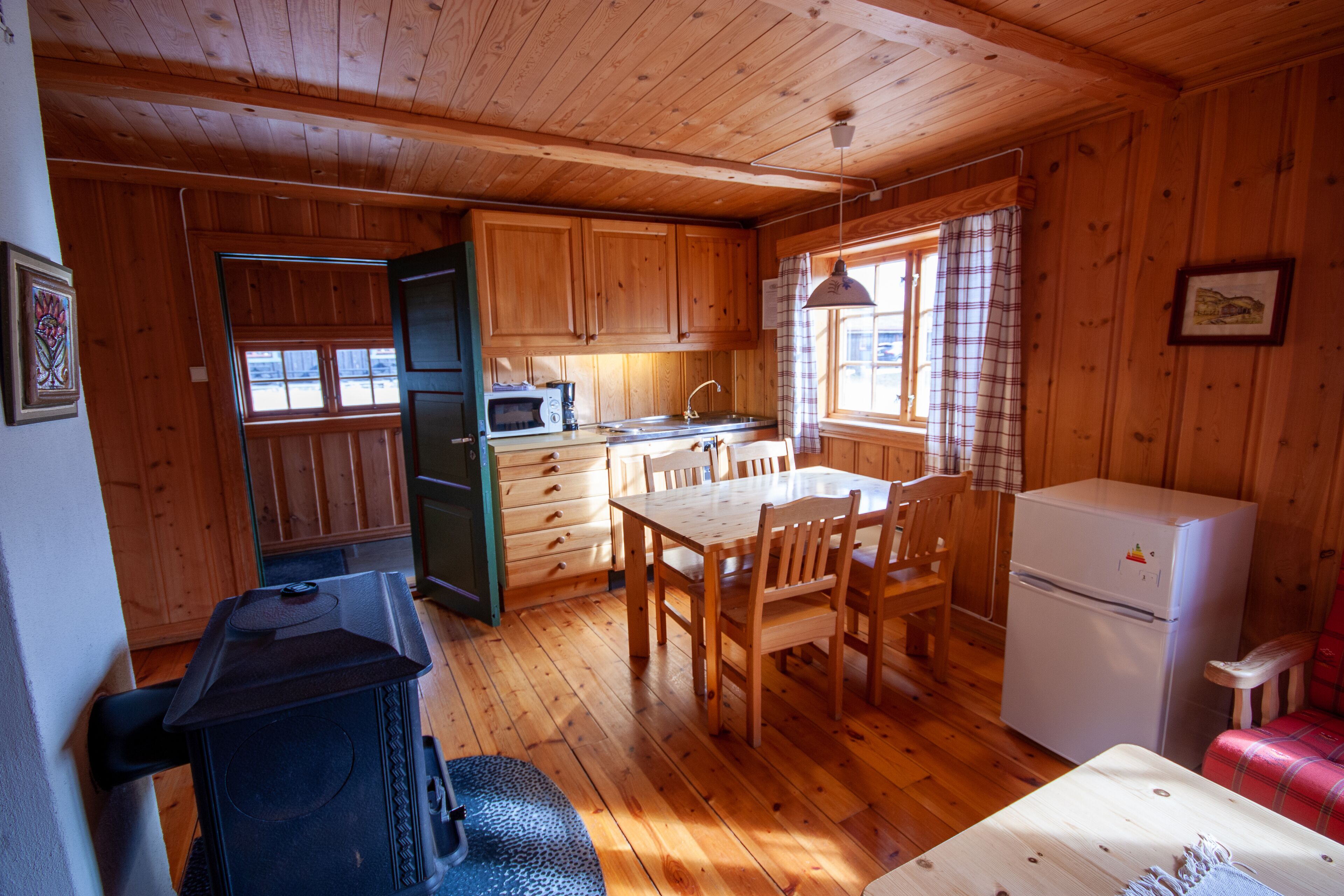 A wooden cabin interior with a kitchen, dining area, and a small living space.