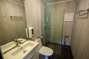 Un baño con ducha de vidrio, lavamanos blanco y retrete.