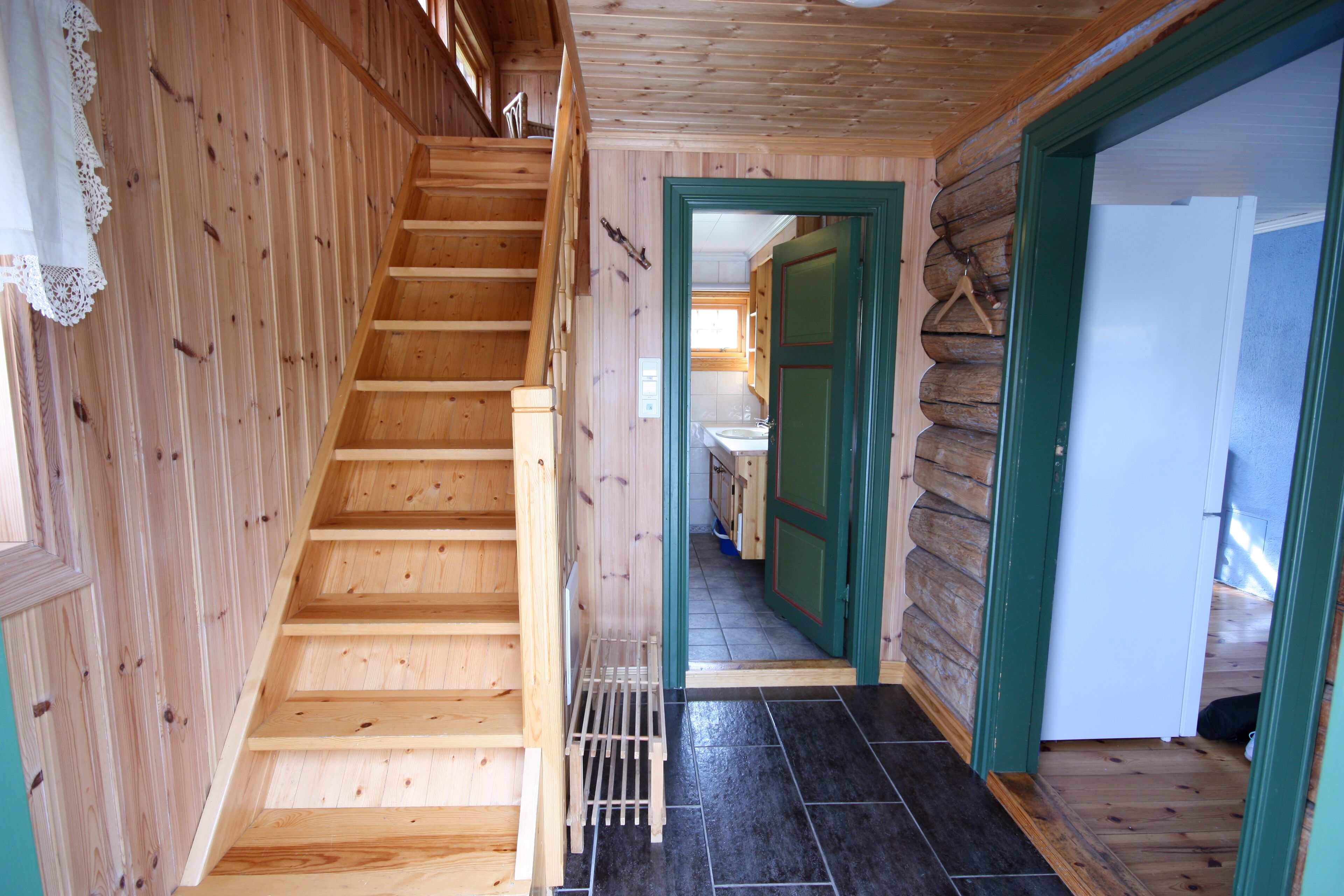 Una escalera de madera que conduce a una habitación con piso de baldosas y una puerta verde.