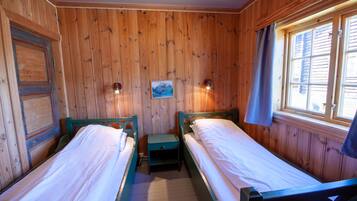A room with wooden walls and two single beds with green headboards.