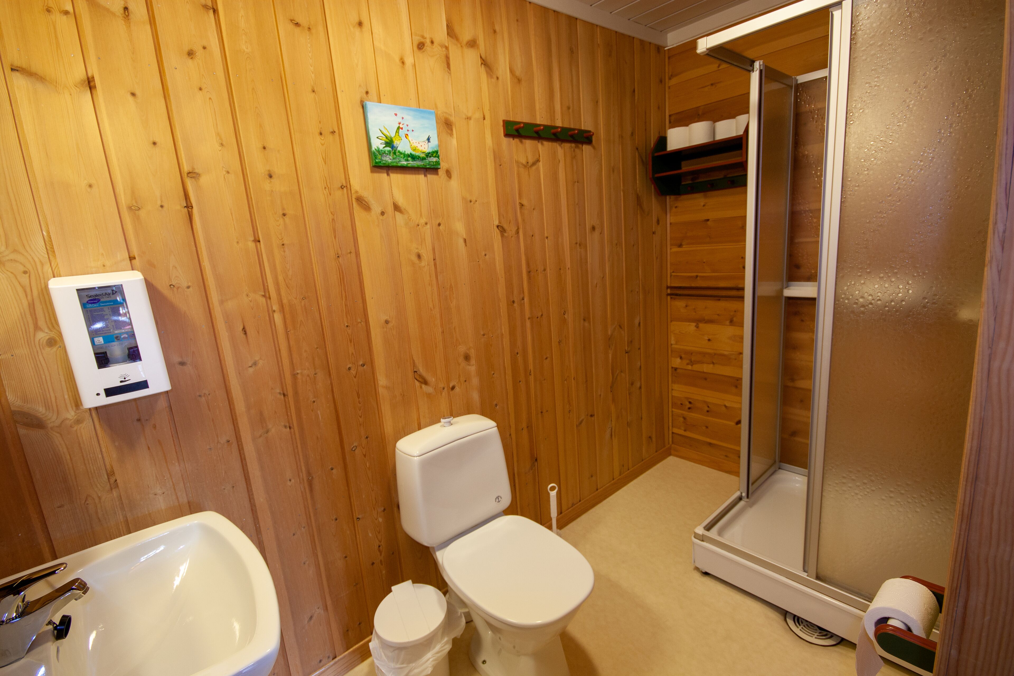 Un baño con paredes de madera, un inodoro, un lavabo y una ducha.