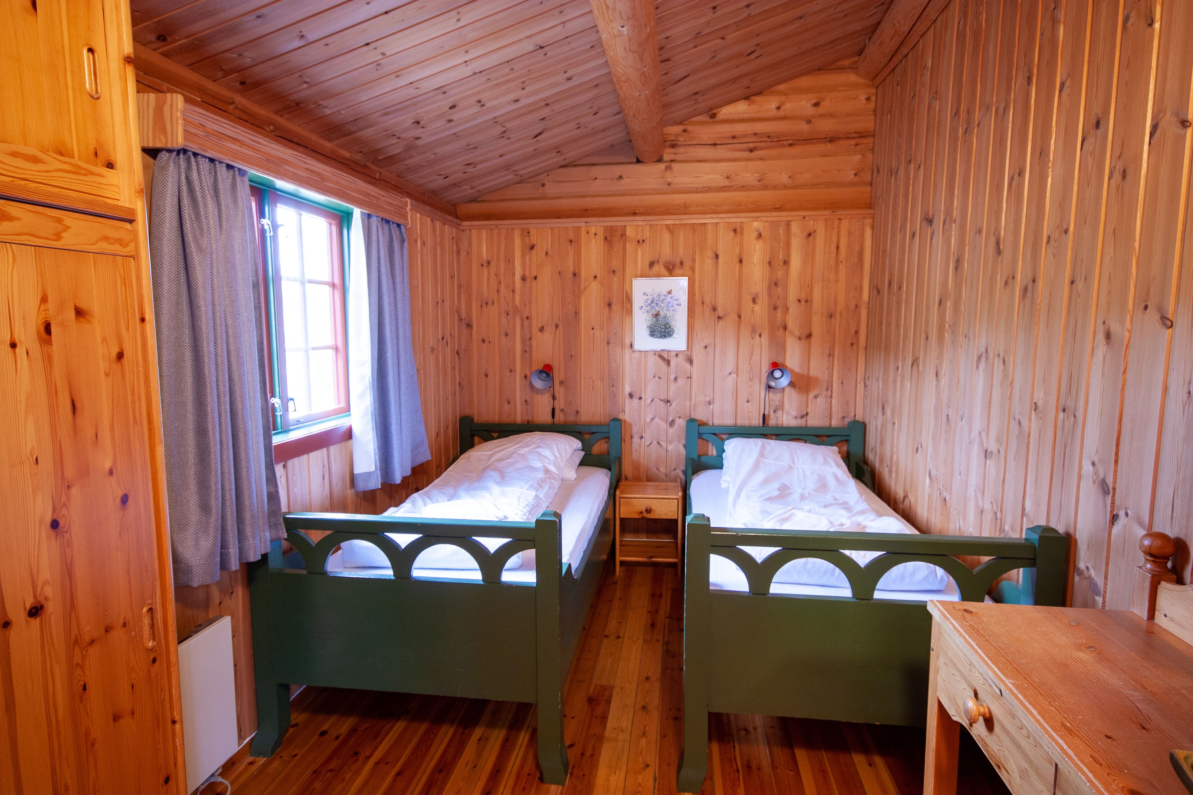 Una camera in baita di legno con due letti, un tavolino e una finestra con tende.