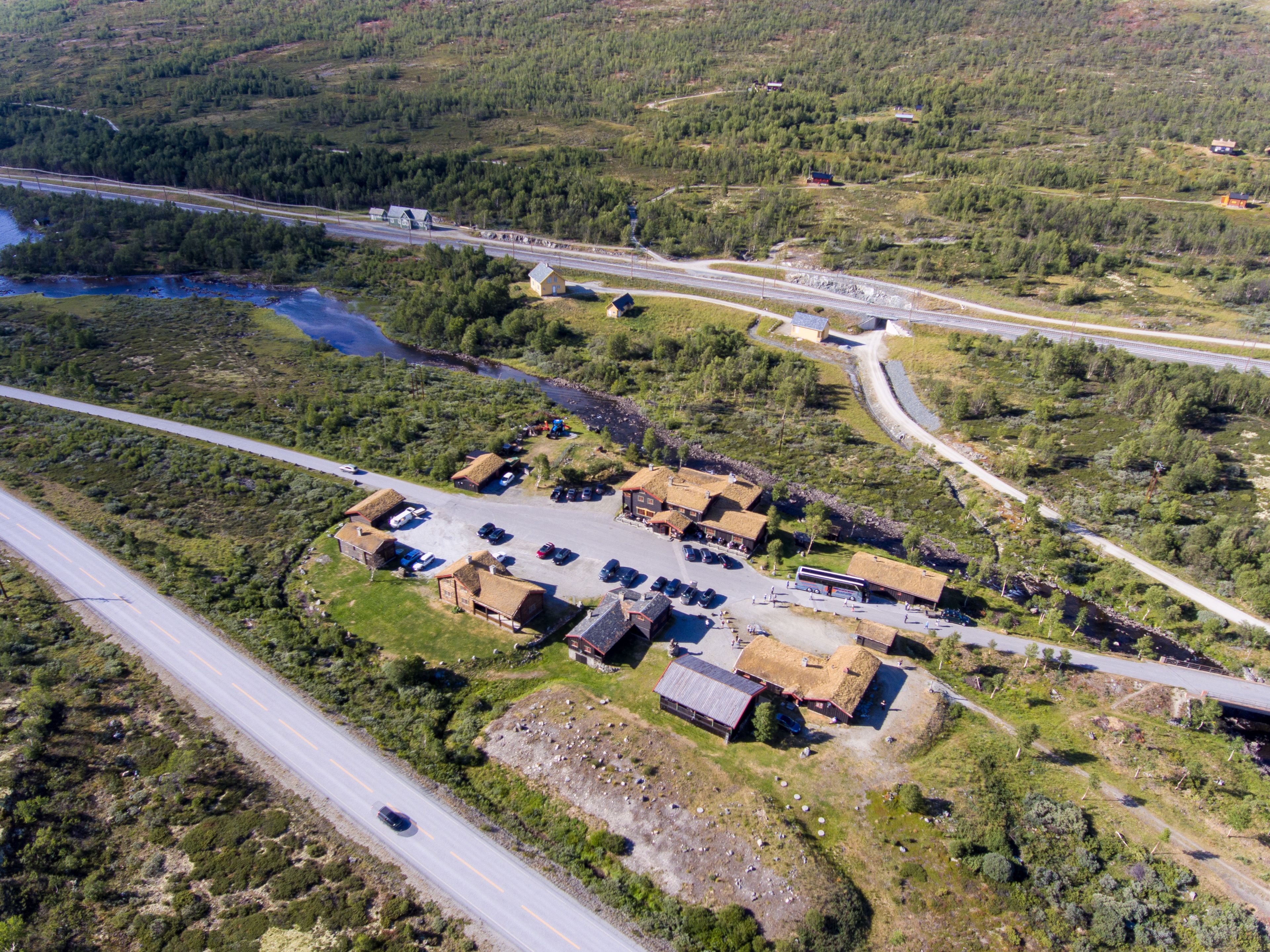 An aerial view of a rural area with a small settlement featuring several buildings, a road, and a river.