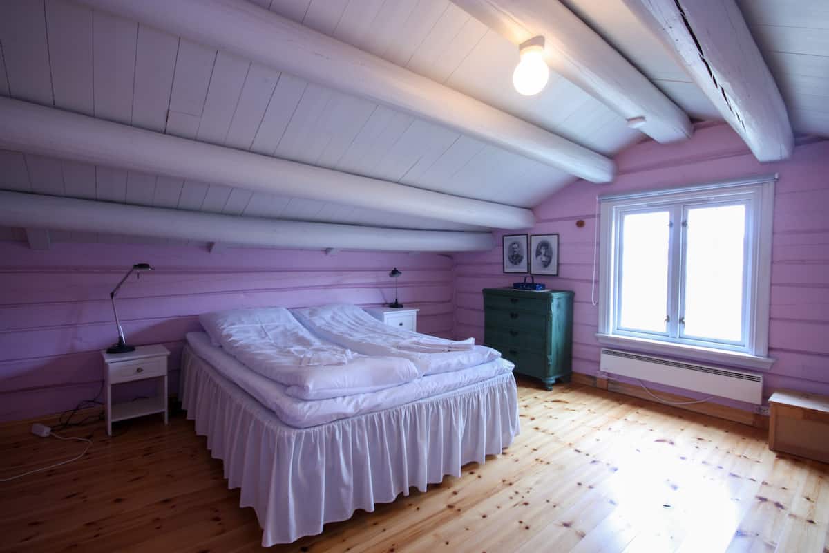 A bedroom with a bed, a dresser, a nightstand, a window, and a ceiling with exposed beams.
