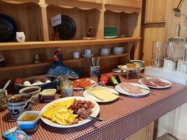Un bufé de desayuno con diversos alimentos y una estantería de madera decorativa al fondo.