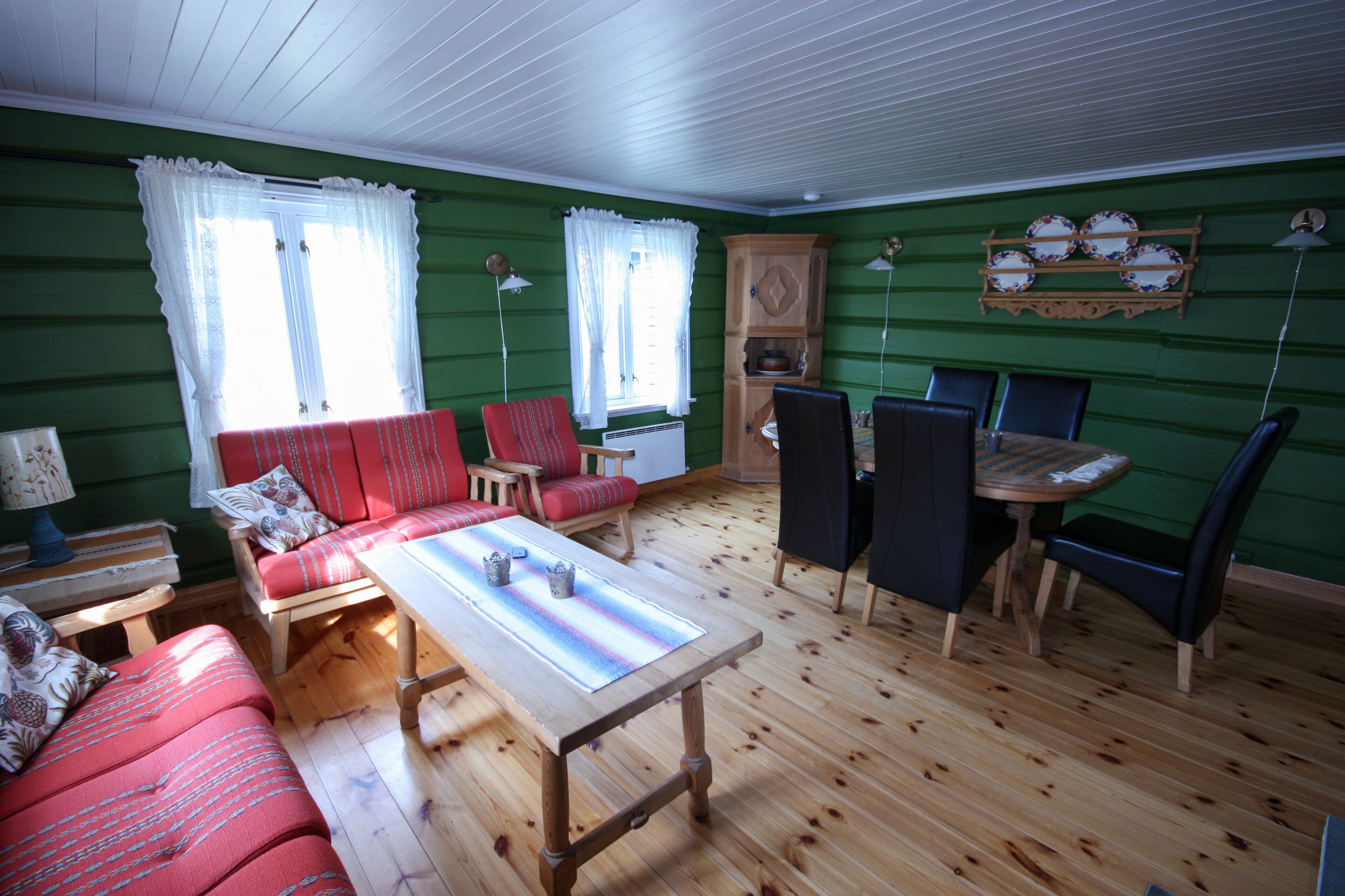 A cozy room with a wooden floor, a red sofa, a dining table, and a cabinet with dishes.