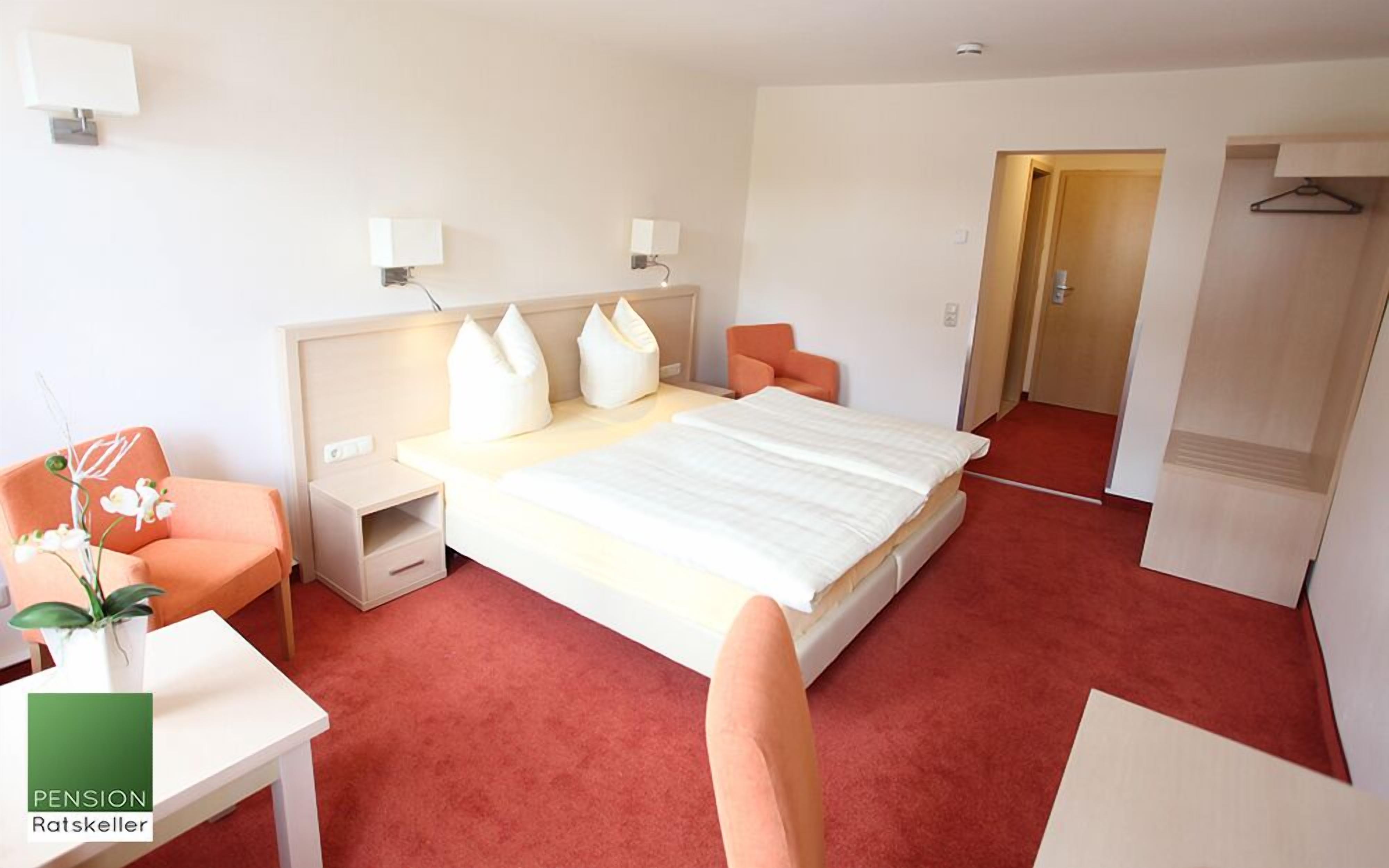 A hotel room with a large bed, two bedside tables, a nightstand, a chair, and a small table with a plant.