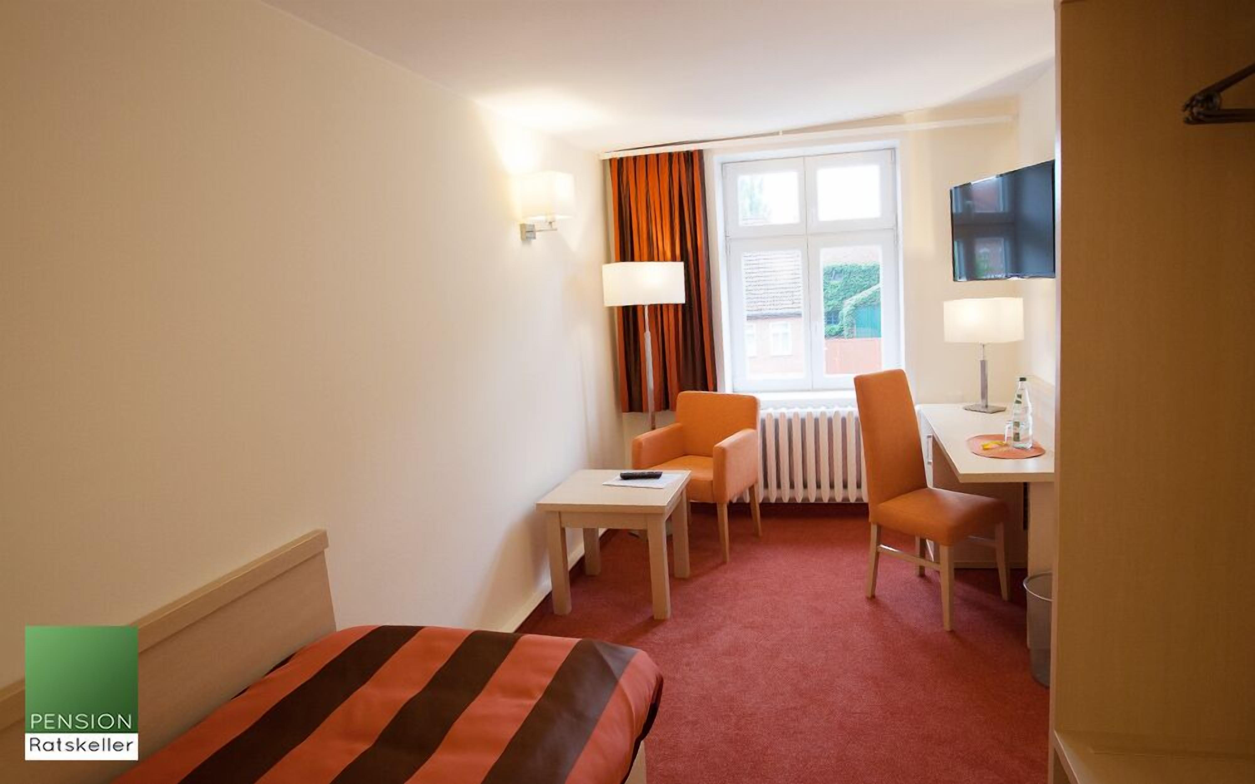 A hotel room with a bed, a desk, two chairs, a TV, and a window with curtains.
