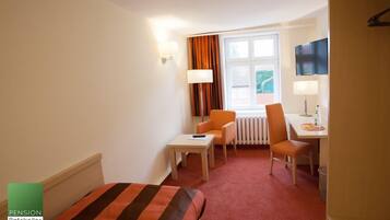 A hotel room with a bed, a desk, two chairs, a TV, and a window with curtains.