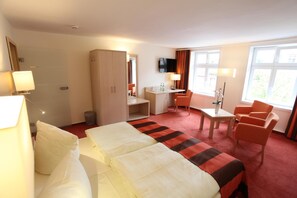 Ein Hotelzimmer mit zwei Betten, einem Schreibtisch, einem Sessel, einem Fernseher und einem Fenster.