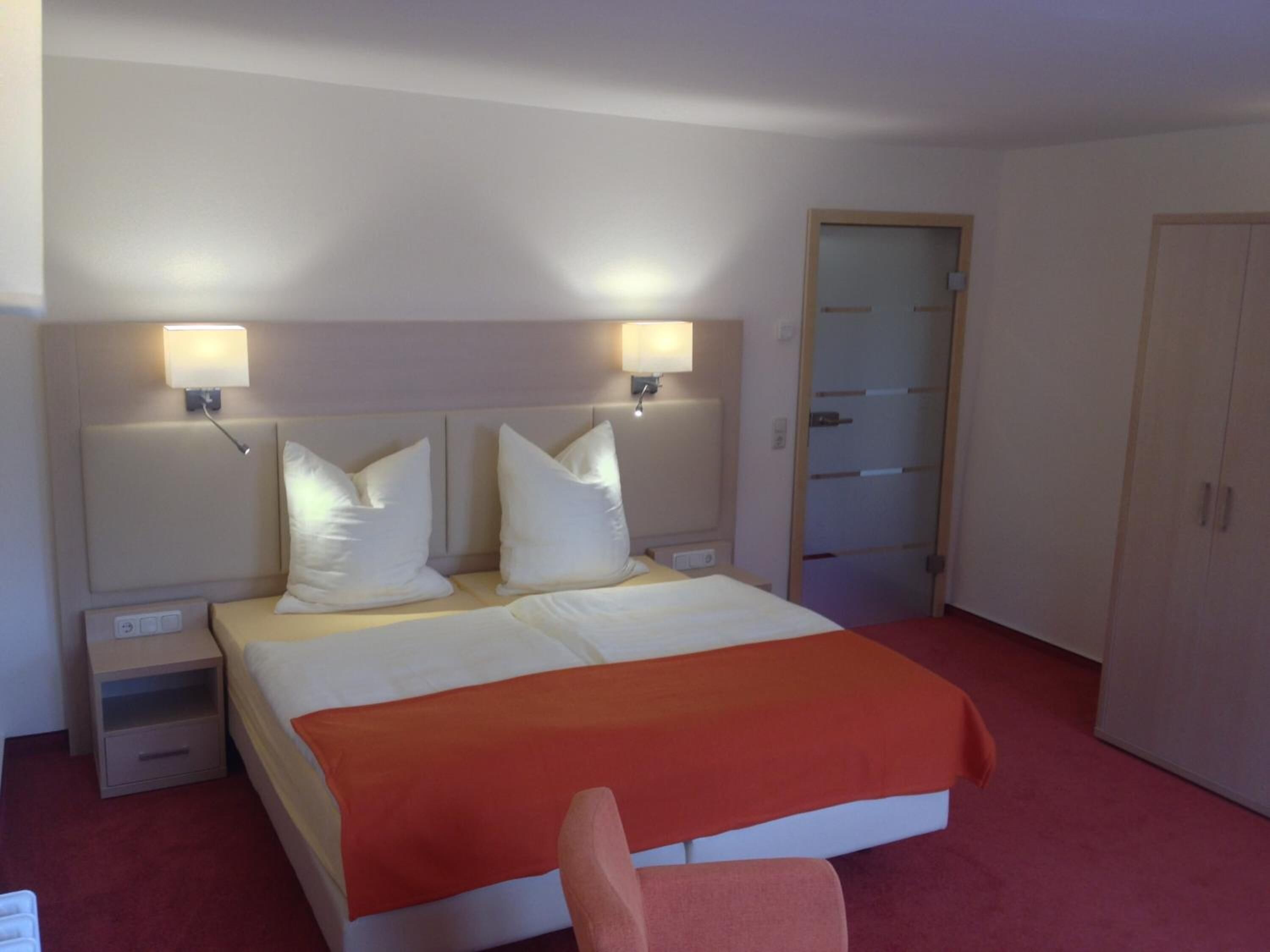 Una camera d'albergo con un letto, due comodini, un armadio e una porta.