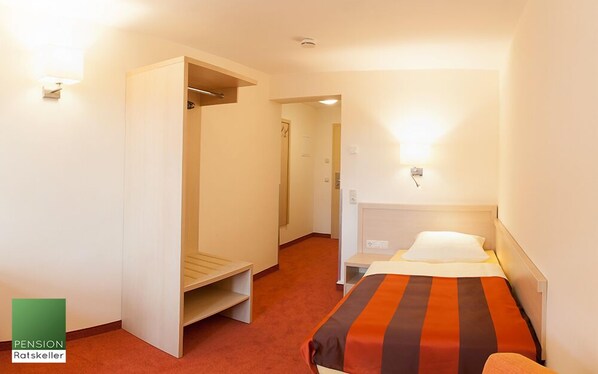 Una habitación de hotel con cama, armario, escritorio y una mesita.