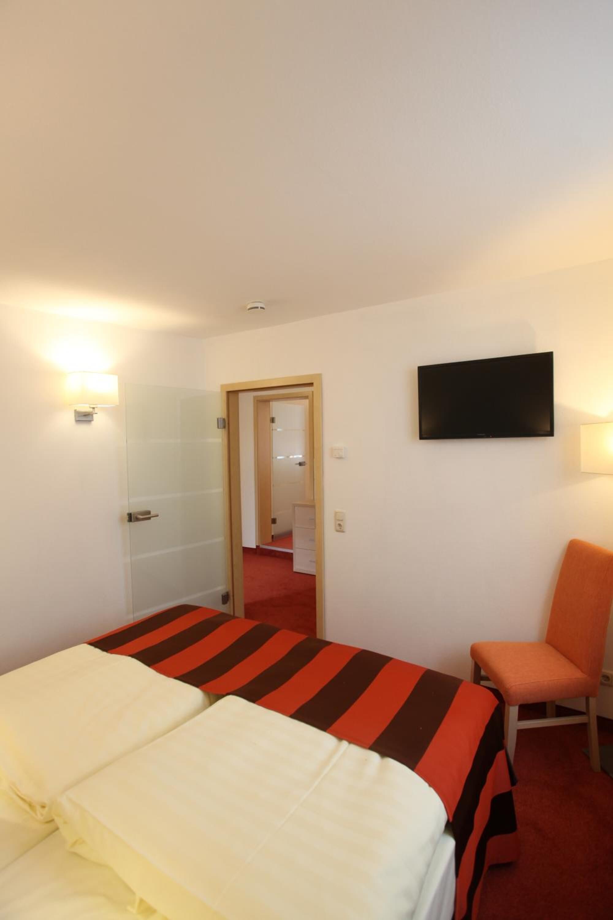 Une chambre d’hôtel avec un lit, une chaise, un téléviseur et une porte donnant sur une autre pièce.