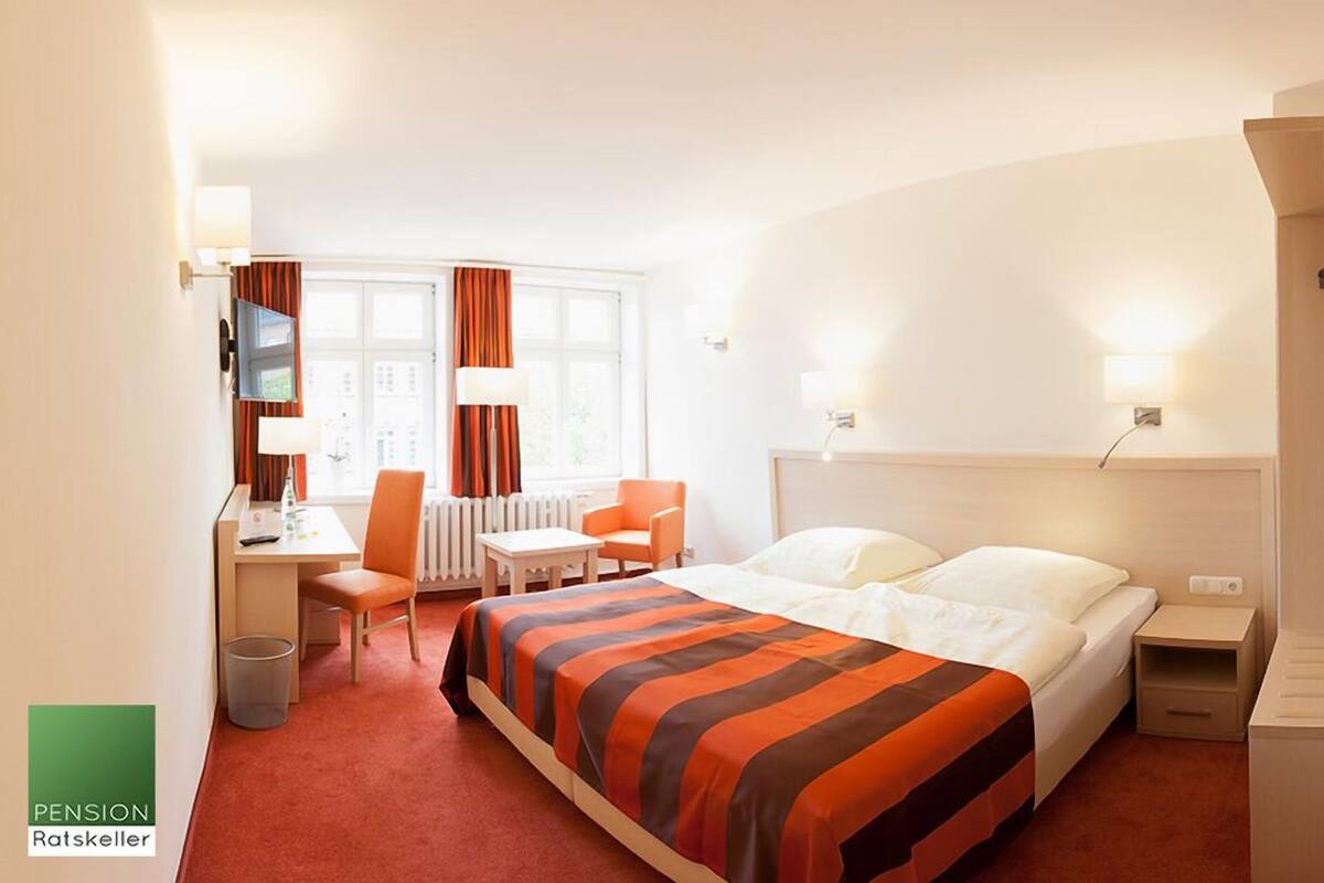 Ein Hotelzimmer mit Bett, Schreibtisch, Stuhl, Fernseher und einem Fenster mit Vorhängen.