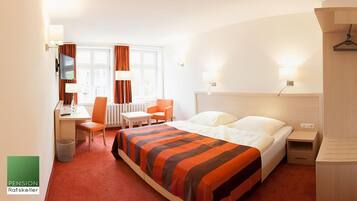 A hotel room with a bed, a desk, a chair, a TV, and a window with curtains.