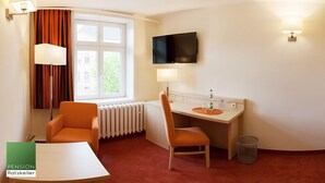 Une chambre d’hôtel avec un lit, un bureau et une chaise, une télévision et une fenêtre avec des rideaux.