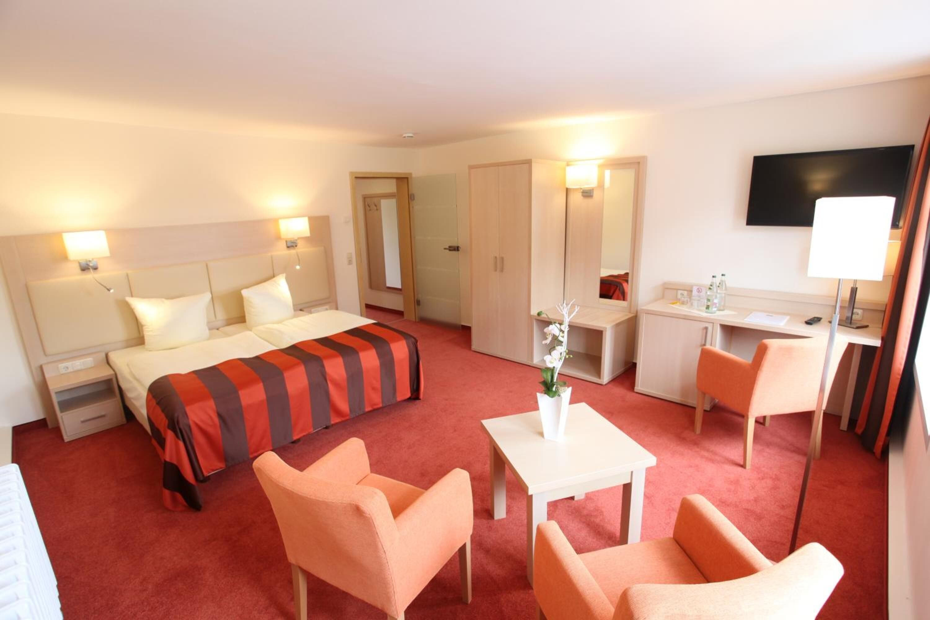 A hotel room with a bed, two chairs, a desk, a TV, and a mirror.