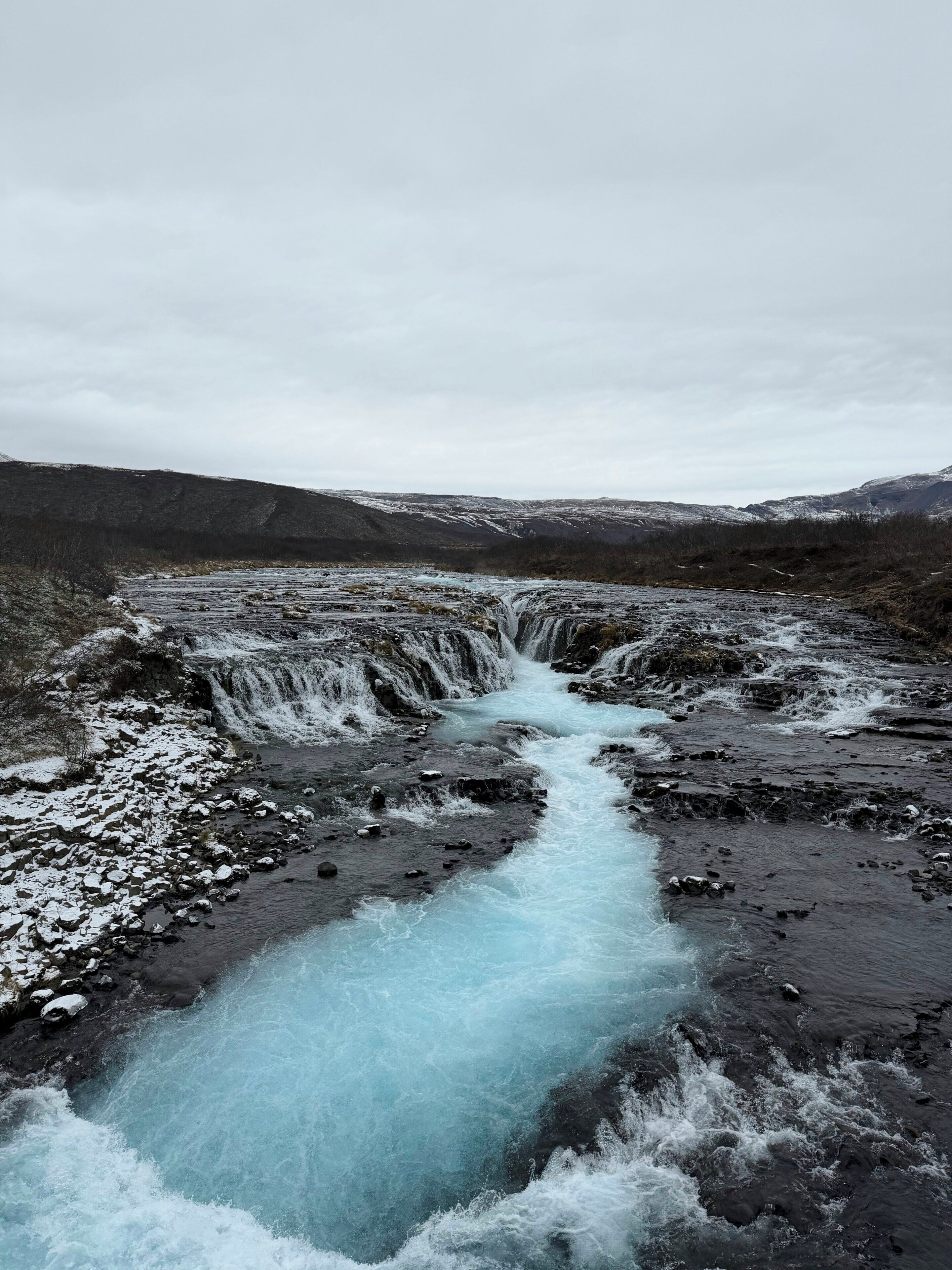 Une rivière qui traverse un paysage rocheux, avec des étendues de terrain enneigées.