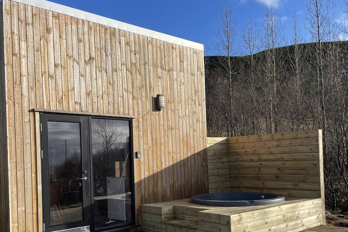 Une cabane moderne en bois, dotée d’une porte d’entrée en verre, d’un bain à remous et d’une terrasse en bois.