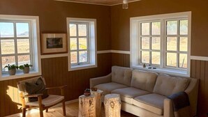 Una habitación acogedora con techo de madera, un sofá color beige, una silla de madera y dos mesas redondas de madera.