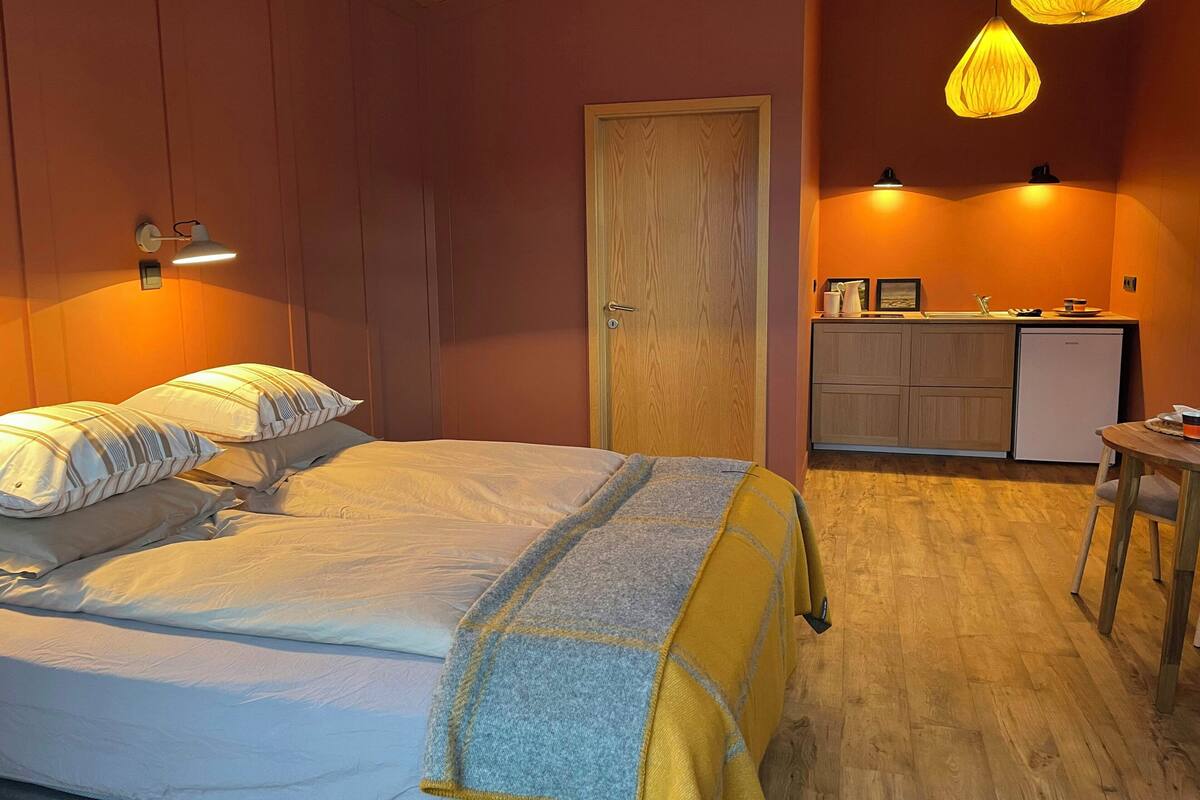 Une chambre à coucher comprenant un lit, des lampes de chevet, une porte en bois, un coin cuisine et une petite table.