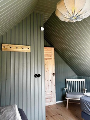 A room with a sloped ceiling, a wooden door, a bench, and a hanging light fixture. - Skard Cottages (Hrunamannahreppur)