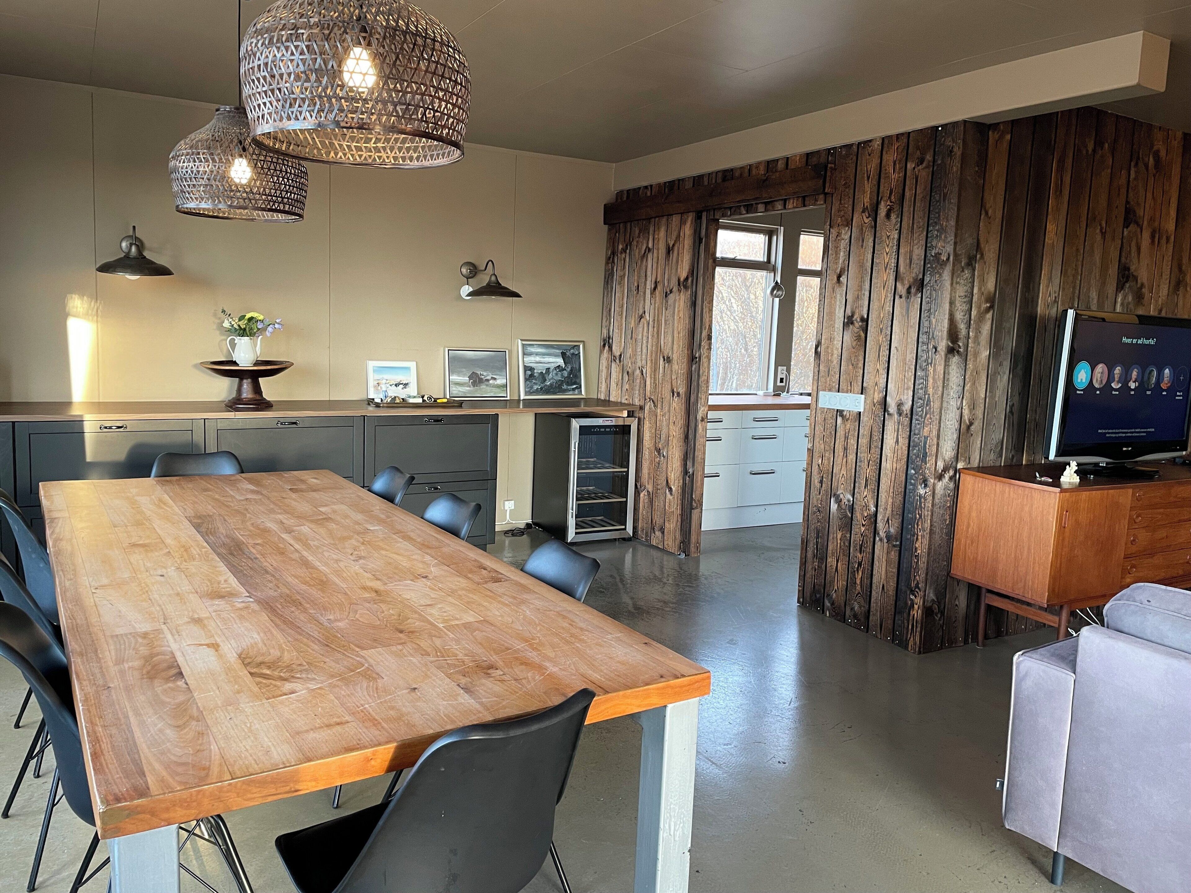 A modern kitchen with wooden cabinets, a dining area with a large wooden table, and a TV on a wooden cabinet.
