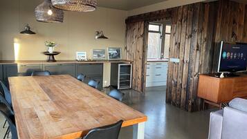 A modern kitchen with wooden cabinets, a dining area with a large wooden table, and a TV on a wooden cabinet.