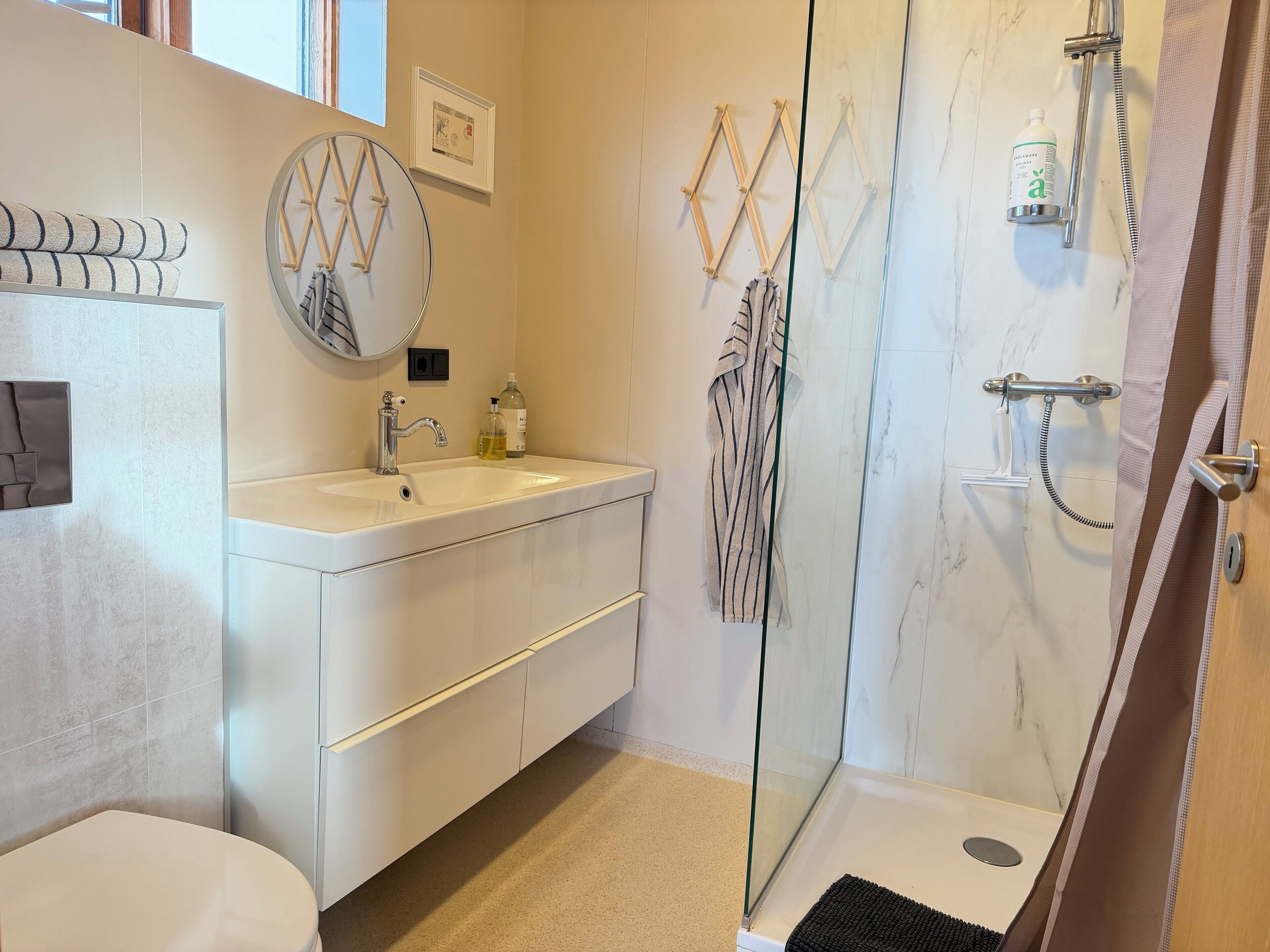 Un baño moderno con lavamanos, espejo y ducha blancos.