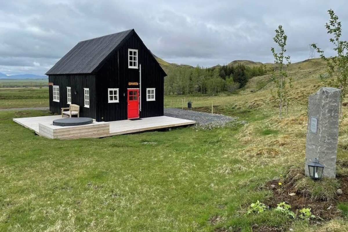 Une maison en bois peinte en noir, avec une porte rouge, un petit porche et un monument en pierre situé à proximité.