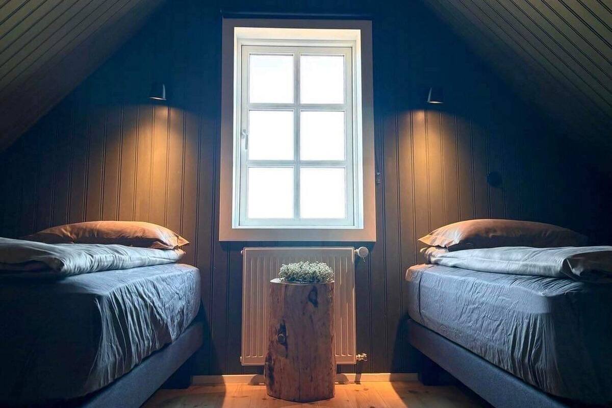 Une chambre mansardée chaleureuse, avec deux lits, une grande fenêtre et un plafond en bois.
