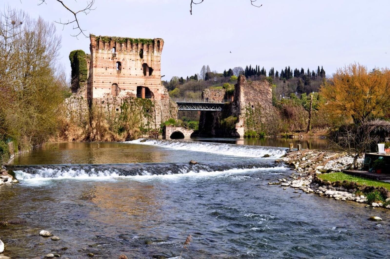 A historic stone bridge over a river, with a castle ruin on the left and a modern bridge on the right.
