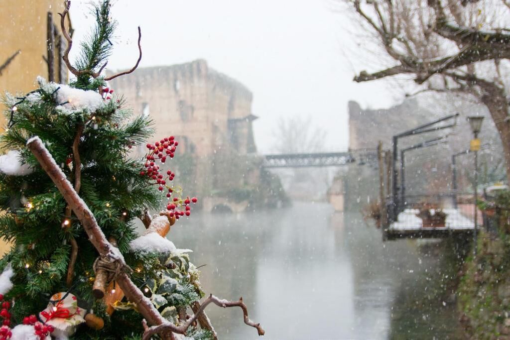 Un árbol de Navidad cubierto de nieve, con adornos y luces, un puente al fondo y un río.