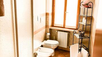 Ein kleines Badezimmer mit Toilette, Bidet und einem Fenster über dem Waschbecken.