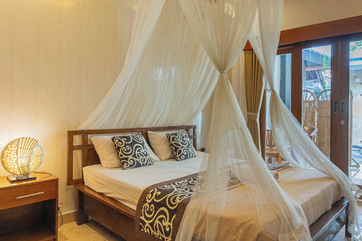A bed with a canopy, a bedside table with a lamp, and a view of the outside.